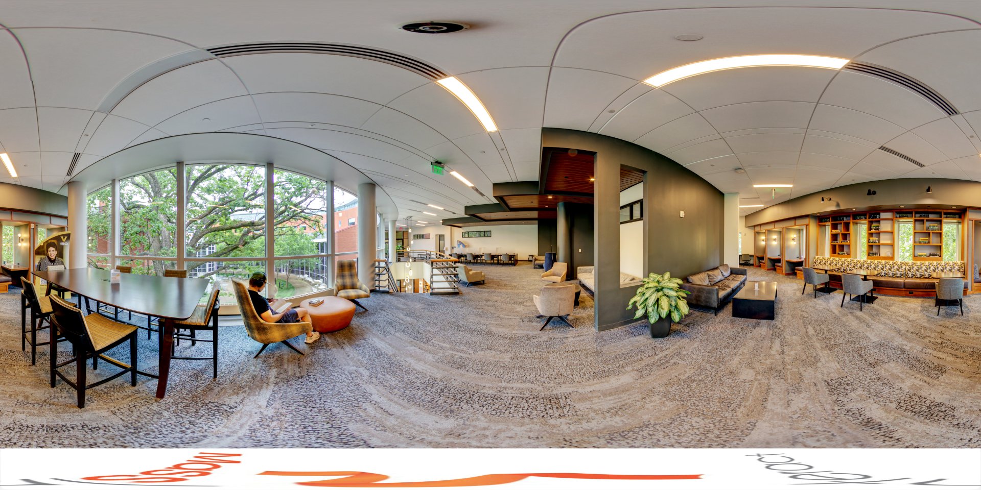 A panoramic view of a modern library's second floor featuring large windows overlooking trees, with various seating options including lounge chairs and long tables. The space includes private study areas, bookshelves, and a staircase leading to the lower level.